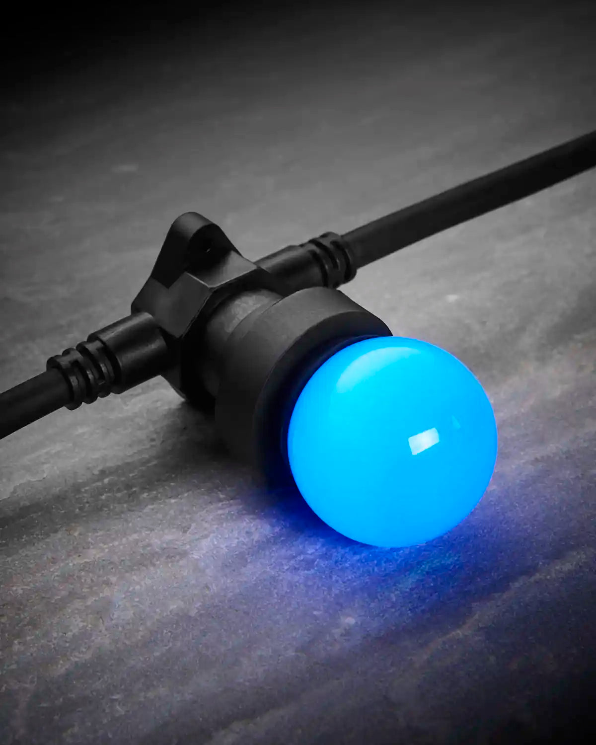 Close-up of a blue E27 LED bulb fitted into a black festoon belt on a dark stone-effect surface.