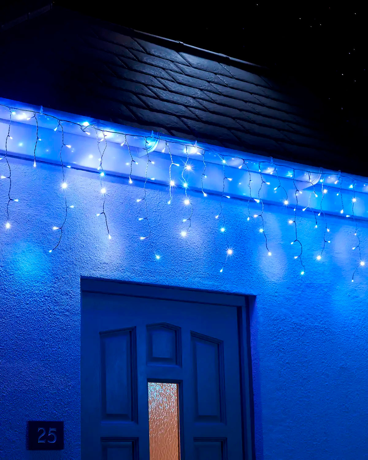 Blue and white icicle lights displayed along a roofline above a front door at night.