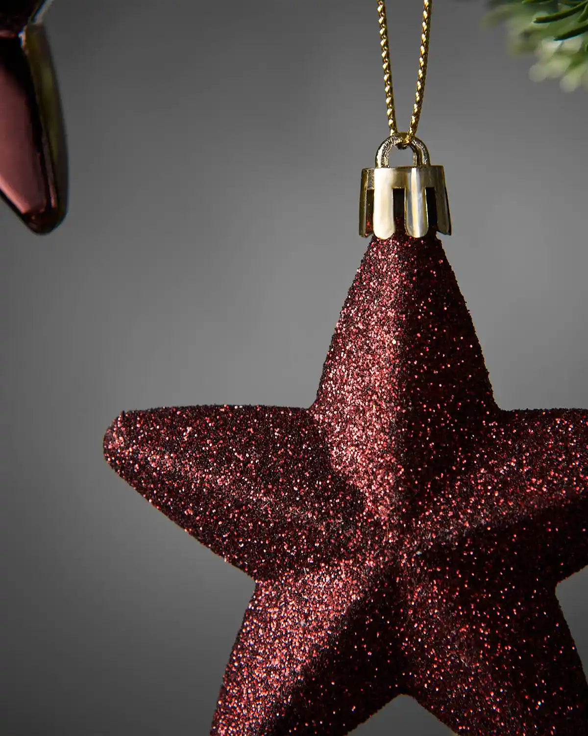 Detailed close-up of a burgundy 7cm glitter hanging star showing the textured finish and gold cap.