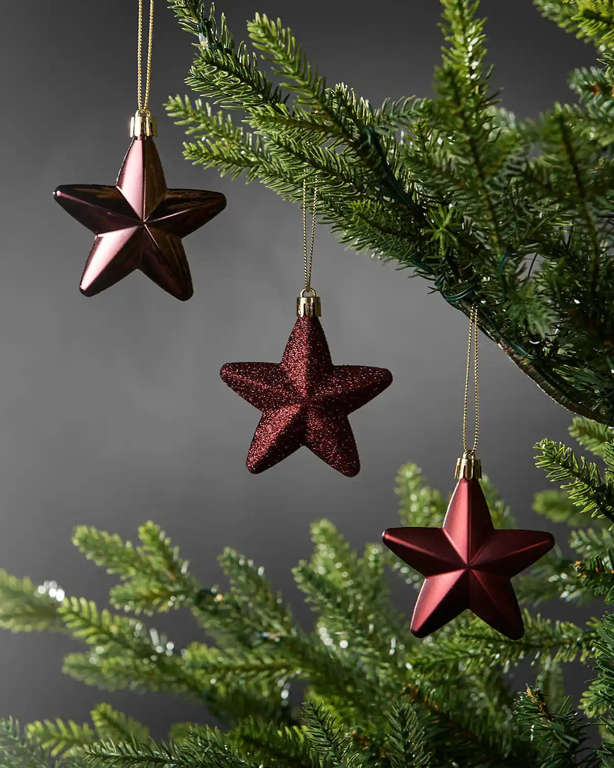 Burgundy 7cm hanging star decorations in shiny, glitter and matte finishes displayed on a Christmas tree.