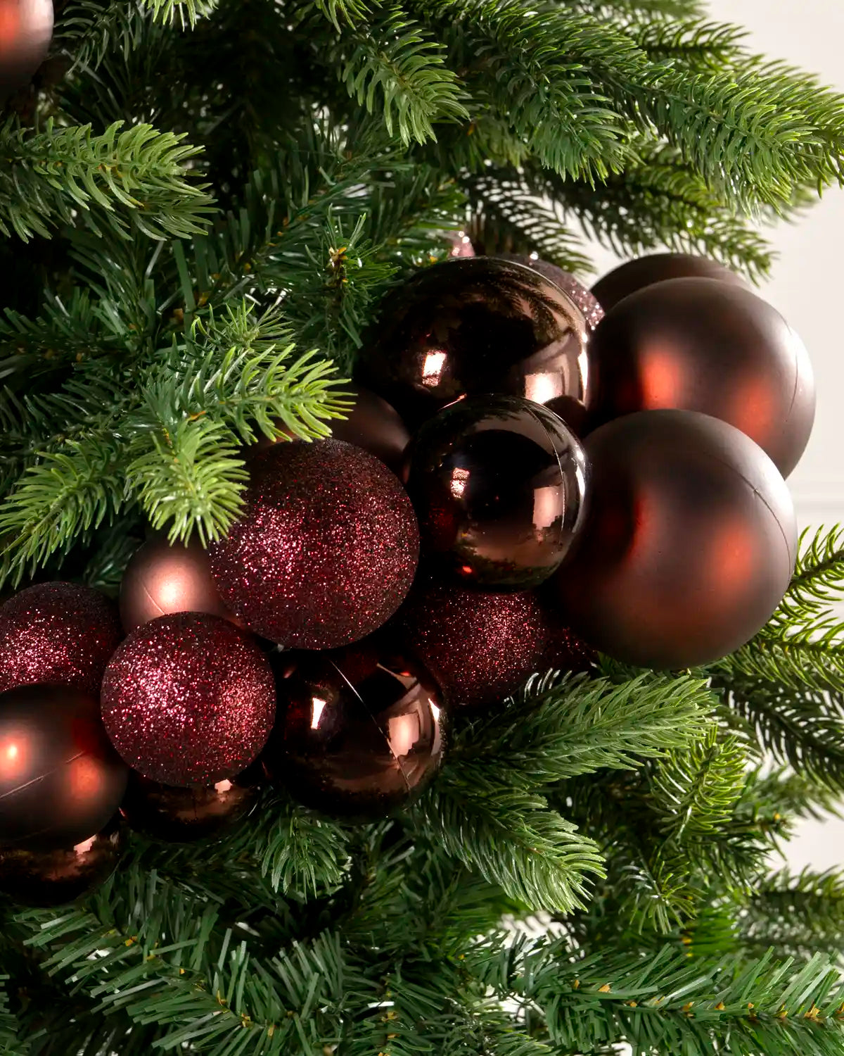 Close-up of burgundy baubles showing shiny, matt and glitter finishes on a Christmas tree.