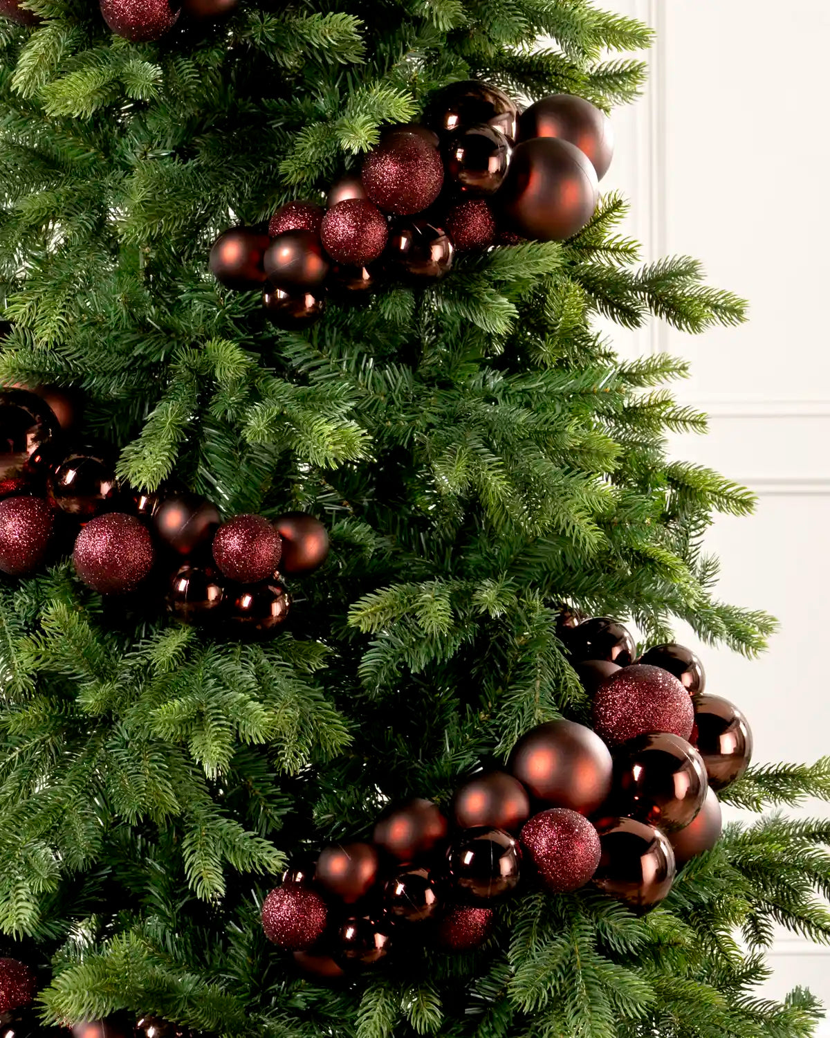 Close-up of burgundy bauble cluster arch on a Christmas tree showing mixed sizes and finishes.