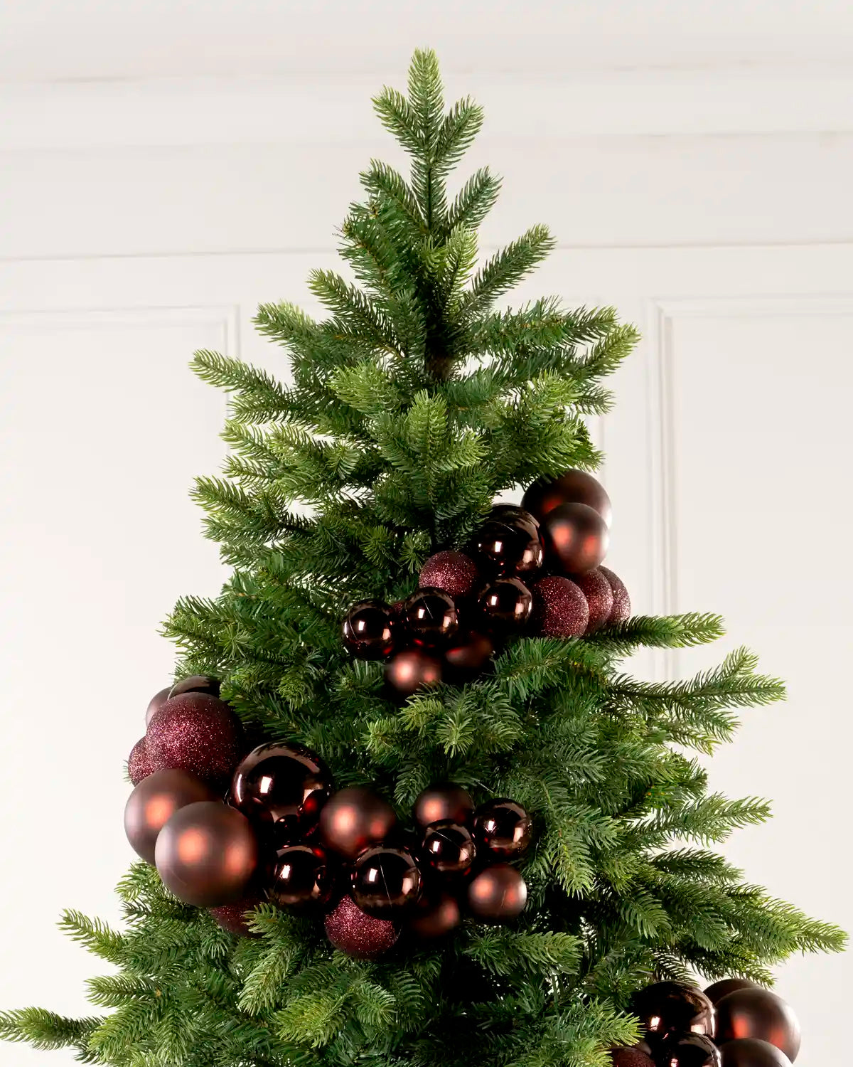 Burgundy bauble cluster arch arranged through the upper branches of a green Christmas tree.