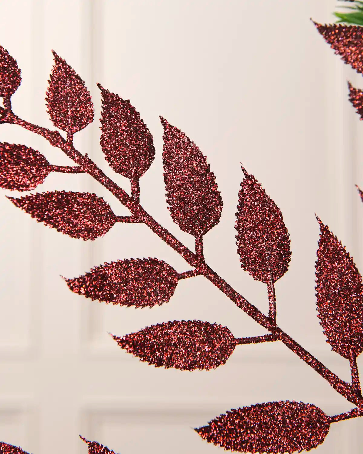 Close-up of the glitter-coated burgundy leaves and branching stem on the Christmas tree spray.