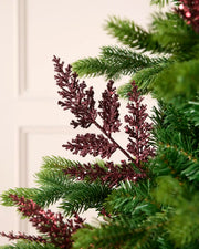 Burgundy glitter leaf pick arranged amongst green Christmas tree branches.