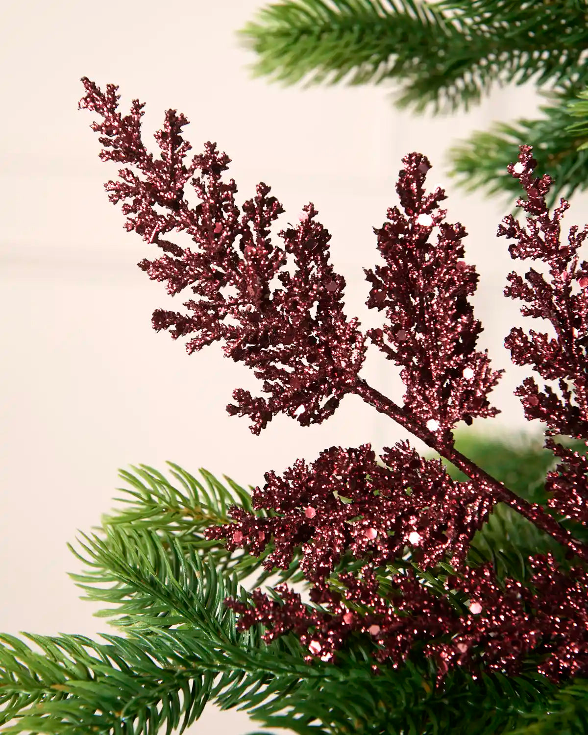 Burgundy glitter leaf pick with detailed branching displayed amongst Christmas tree greenery.