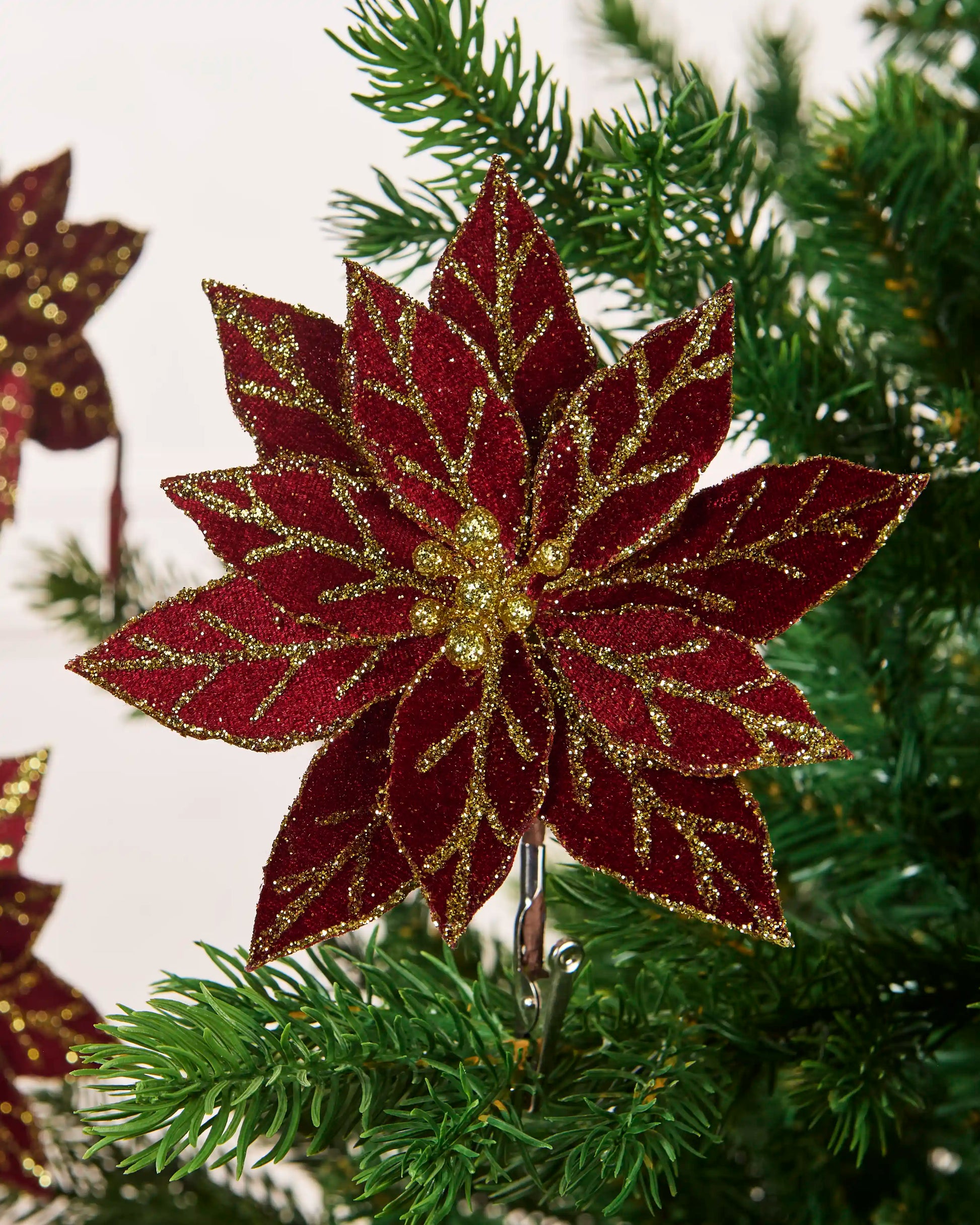 Burgundy 15 cm artificial poinsettia with gold glitter veins and centre clipped to a Christmas tree.