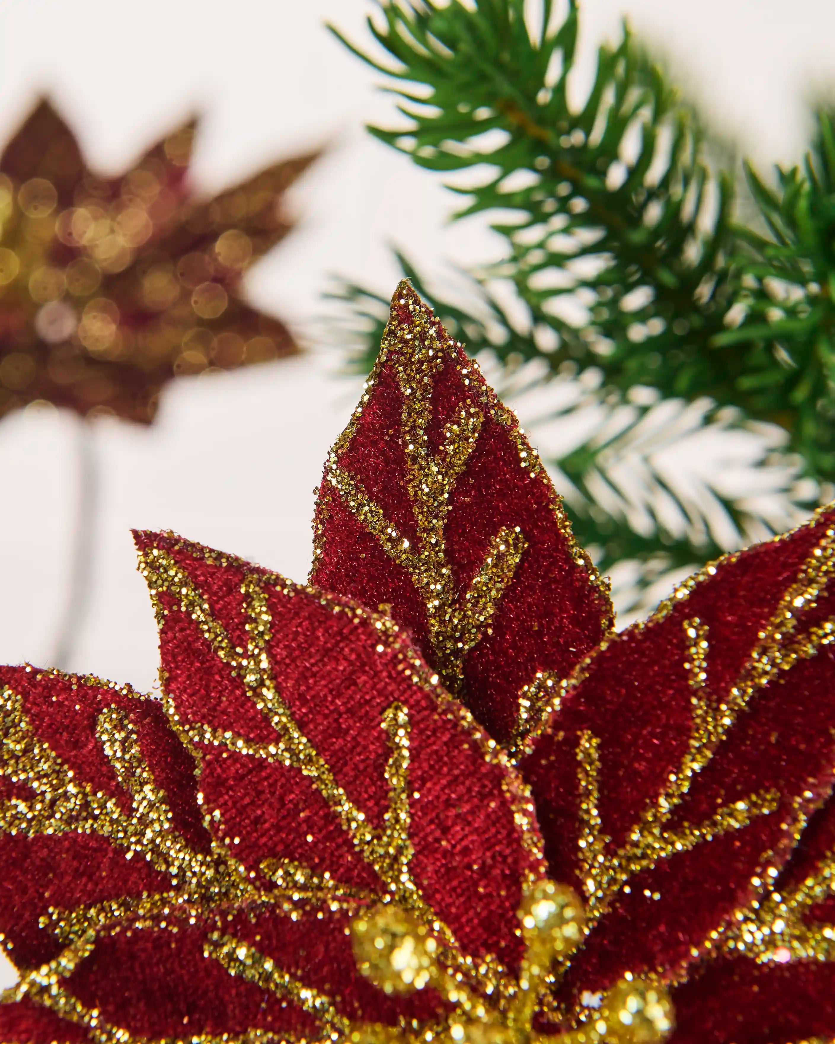 Detailed view of burgundy poinsettia petals with textured fabric and gold glitter edging and veins.