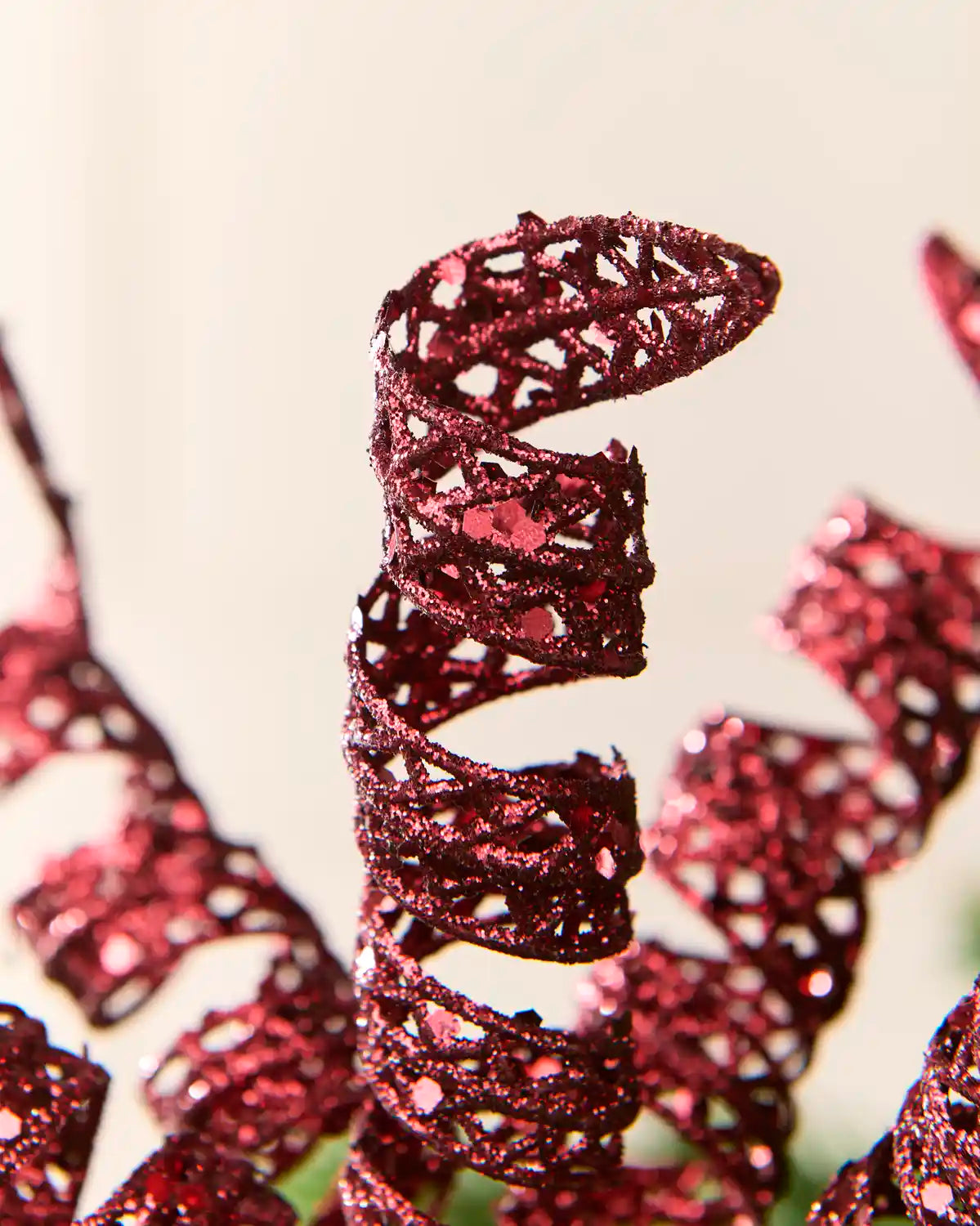 Detailed view of a burgundy glitter spiral pick showing its curled shape and textured reflective finish.