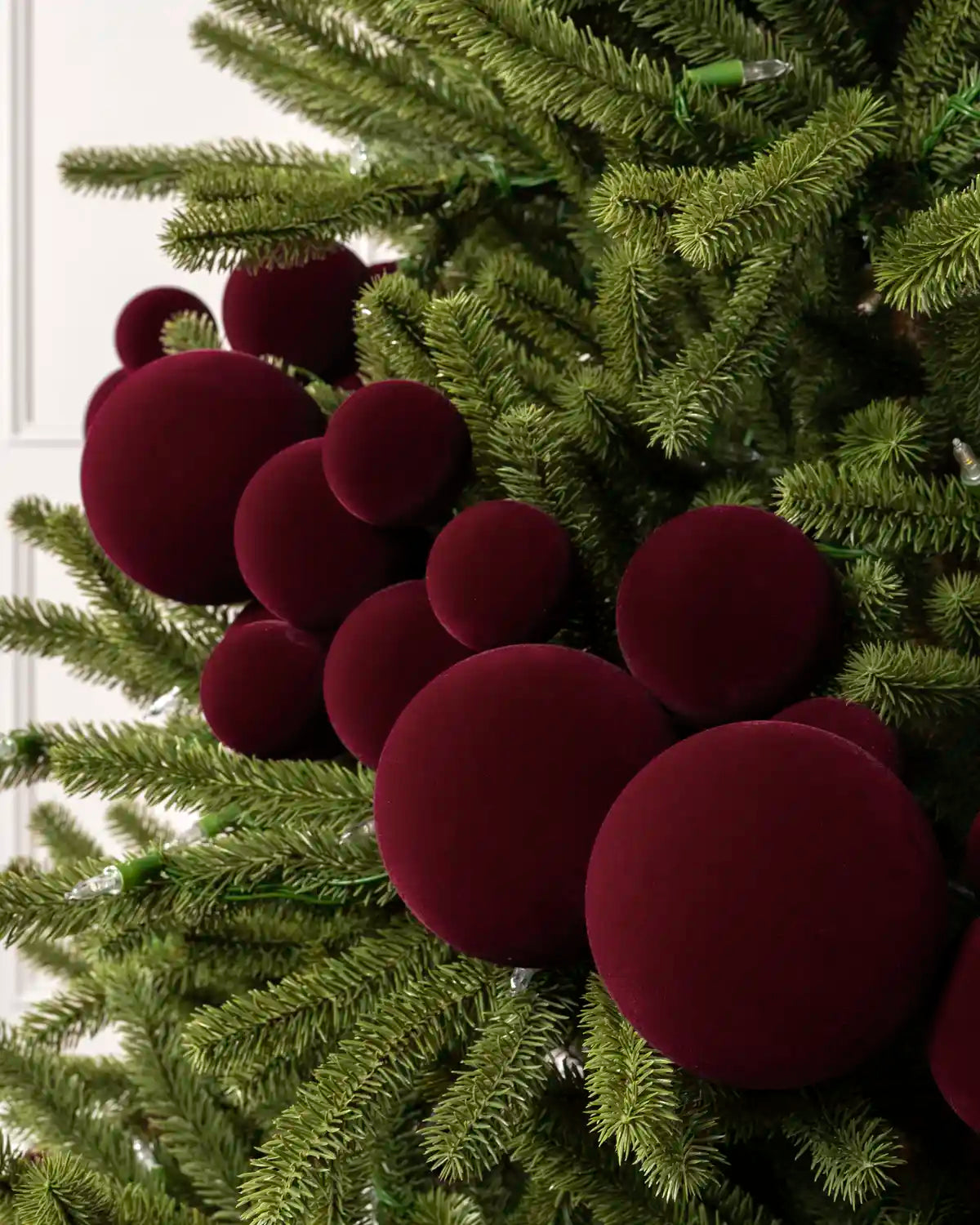 Close-up of burgundy velvet bauble garland on a Christmas tree showing the soft textured finish and mixed bauble sizes.