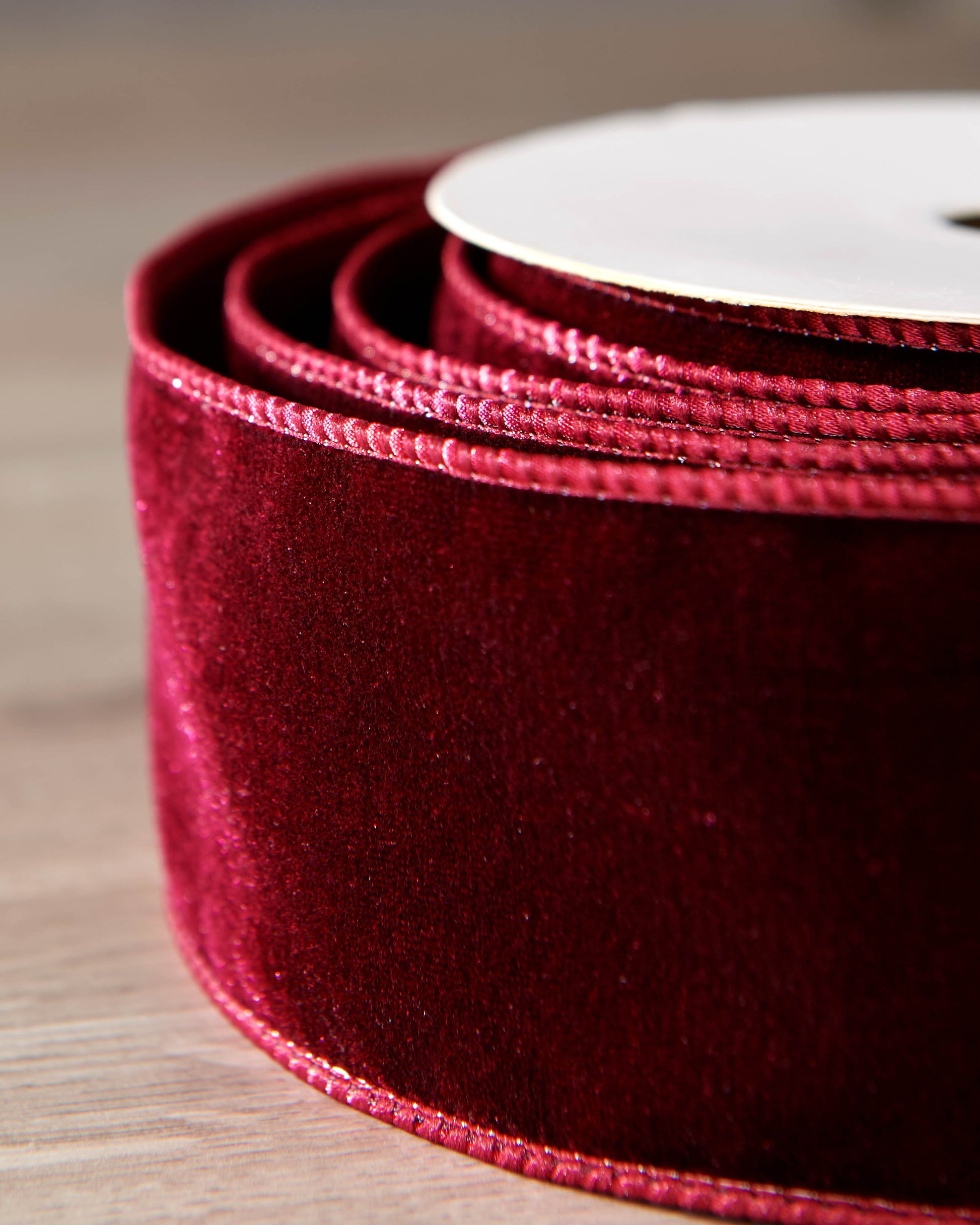 Close-up of burgundy velvet ribbon on a roll, showing the soft texture and wired edge.
