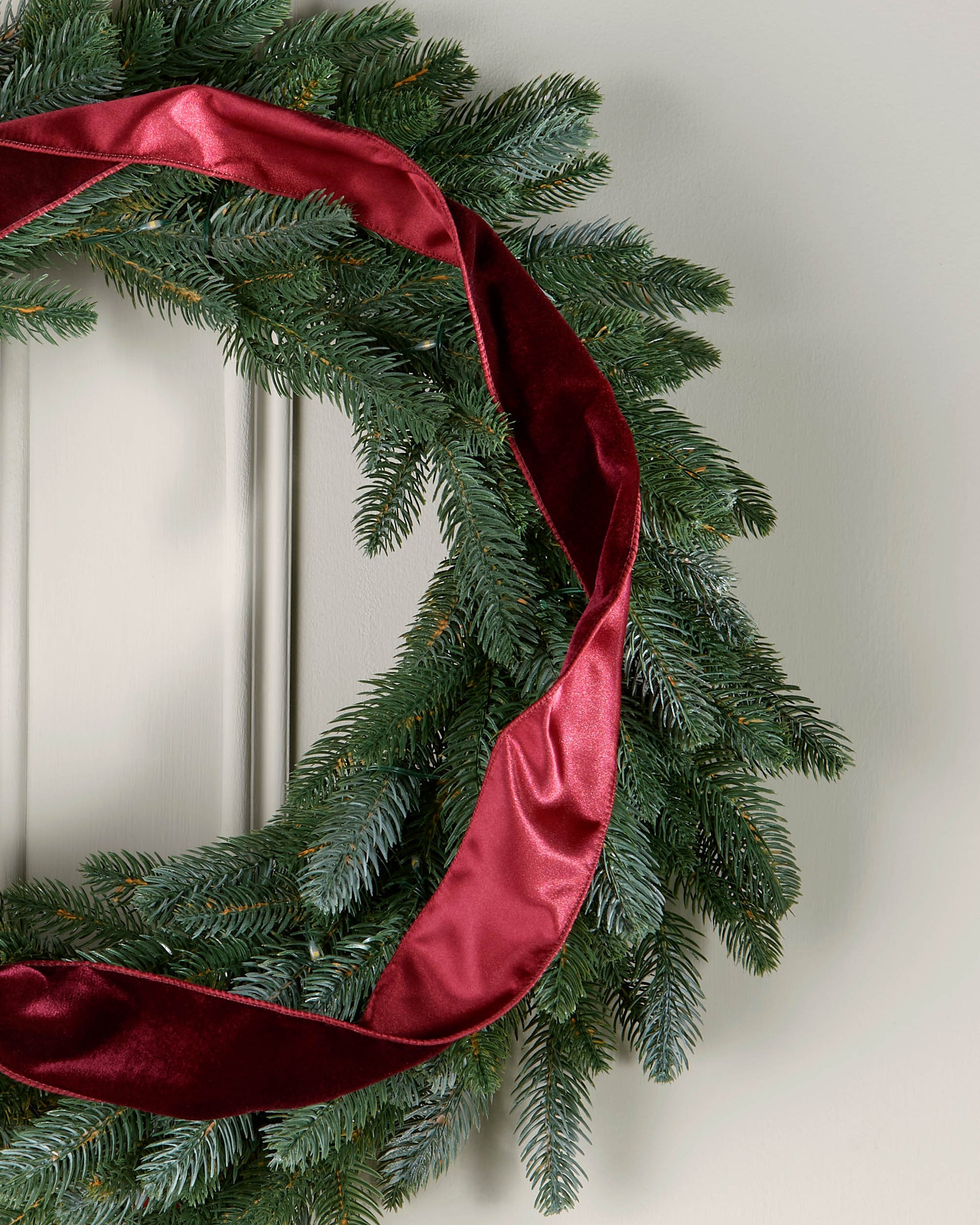 Burgundy velvet ribbon styled in a loose spiral on a green Christmas wreath.