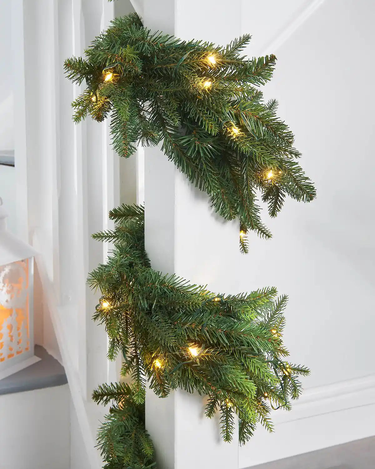 Green garland wrapped around a white staircase banister on against a white wall