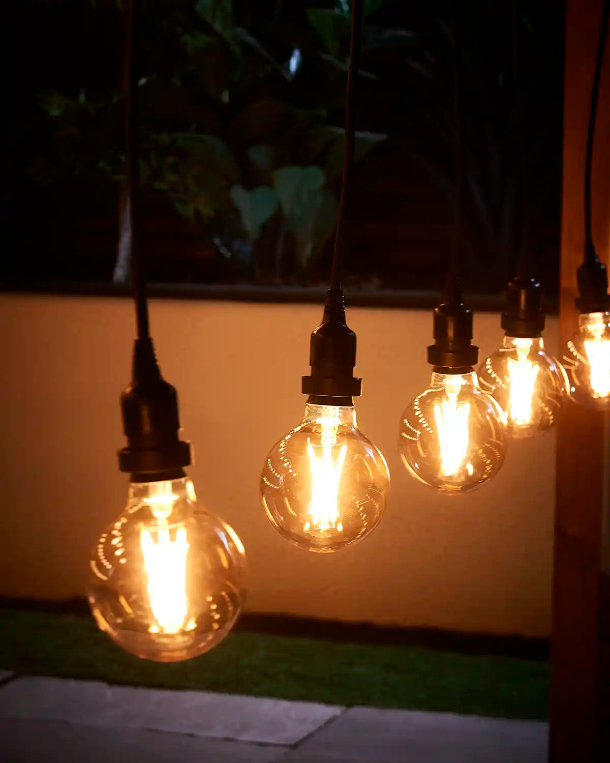 Close-up of hanging E27 festoon pendant bulbs glowing warm white in an outdoor setting.