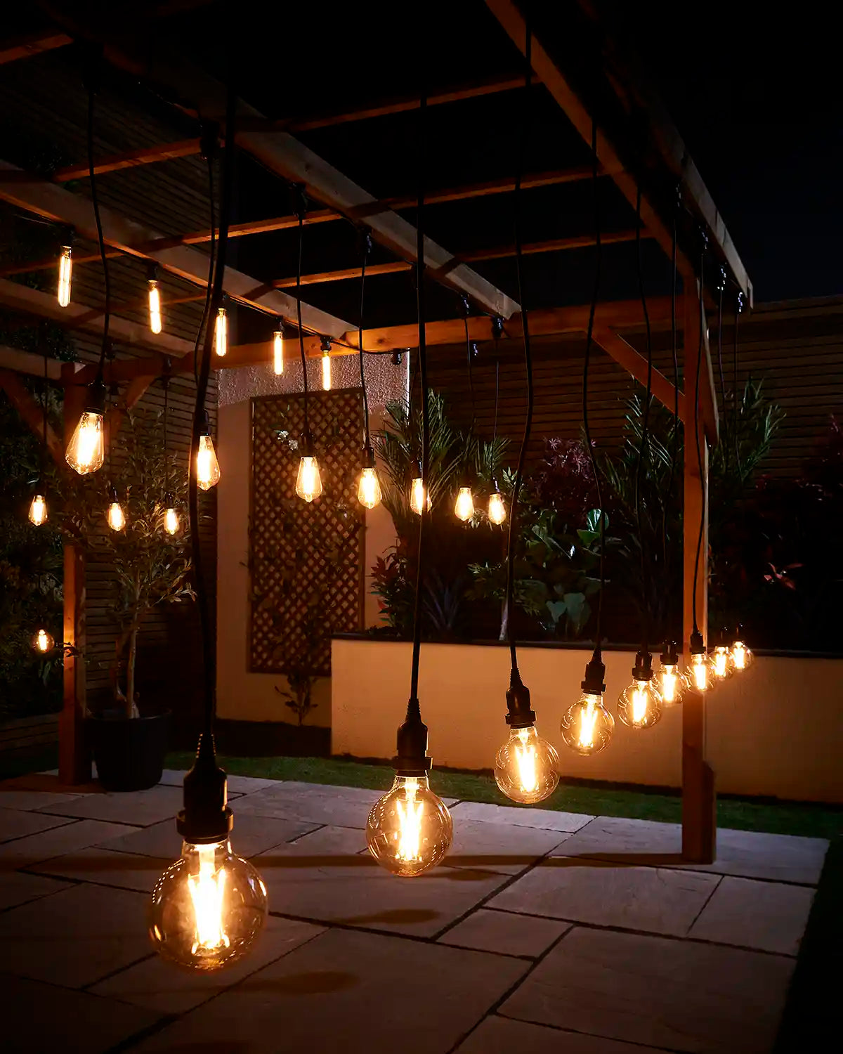 Outdoor festoon pendants with warm filament bulbs hanging from a wooden pergola.