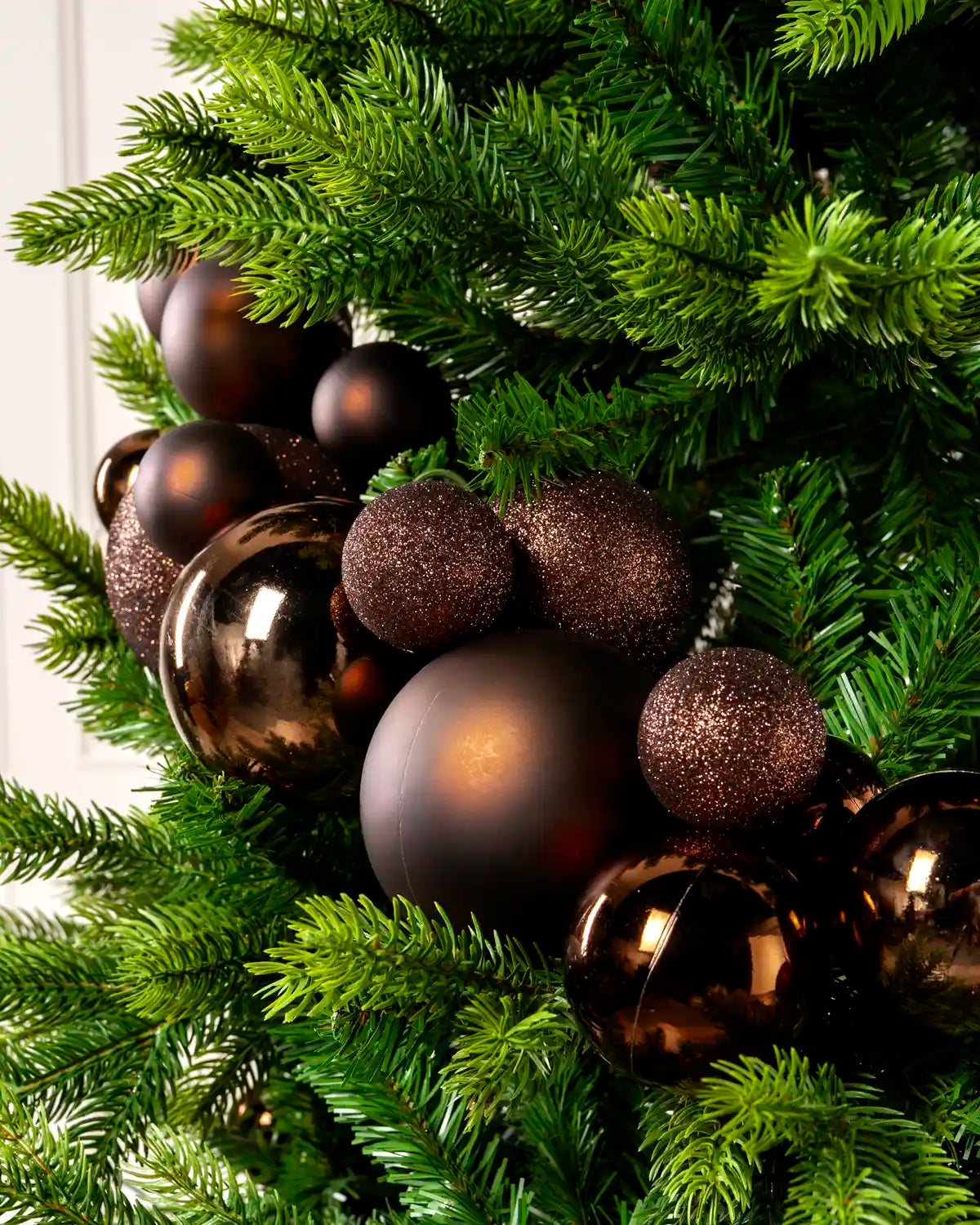 Close-up of espresso bauble garland on a Christmas tree showing mixed sizes, matt, shiny and glitter finishes.
