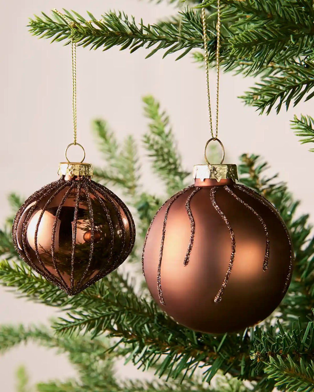 Close-up of espresso onion-shaped and round glass baubles with glitter stripe patterns.