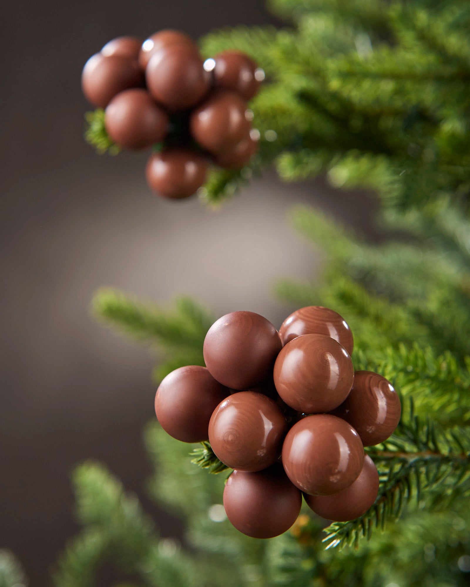 Close-up of espresso glass berry cluster baubles with matt and gloss finishes on a Christmas tree.