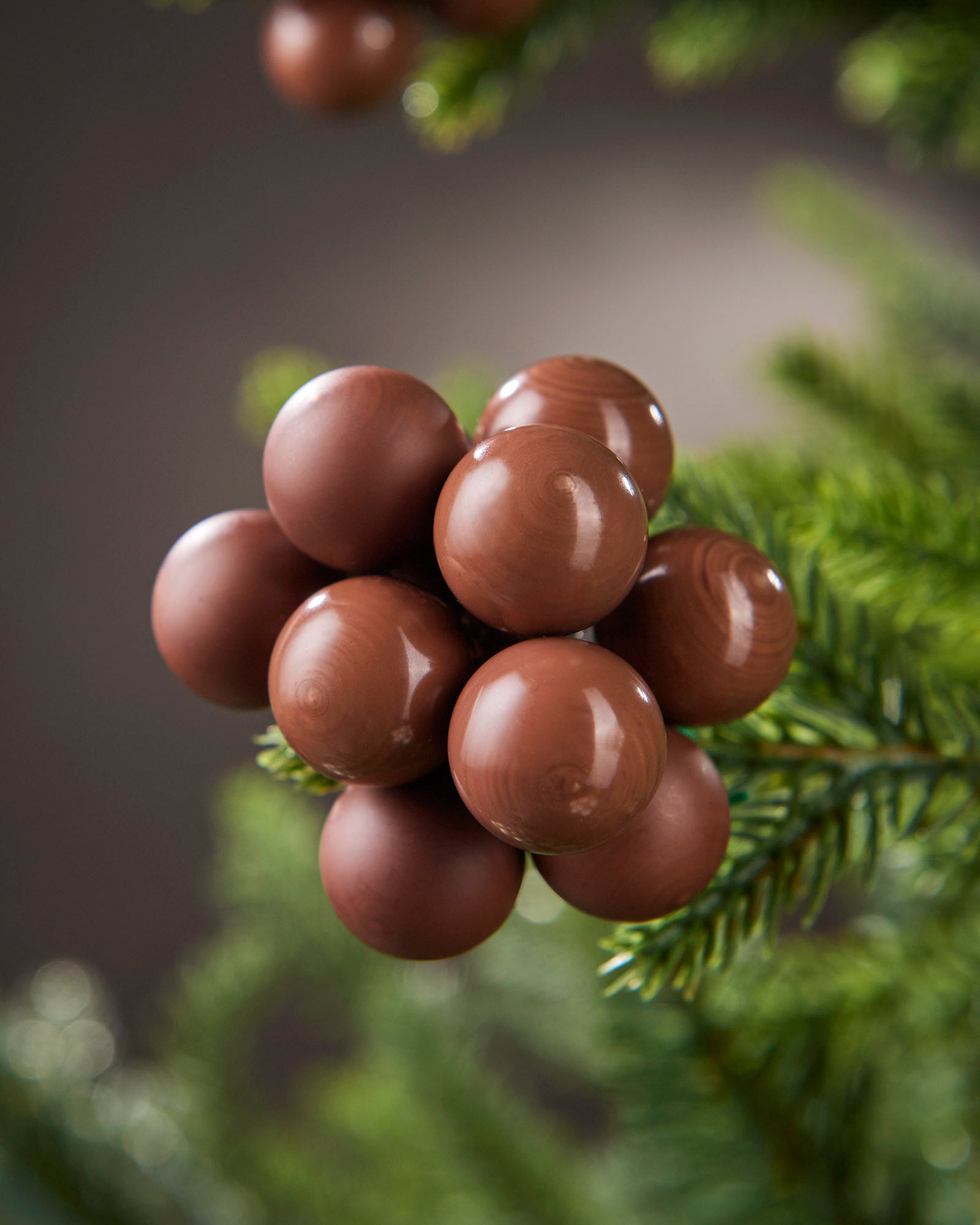 Detailed close-up of espresso glass berry cluster baubles nestled among green tree branches.