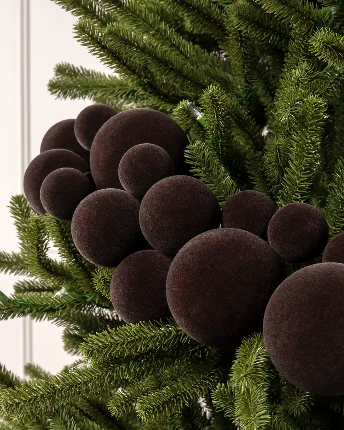 Close-up of espresso velvet bauble garland on a Christmas tree showing the soft textured finish and mixed bauble sizes.