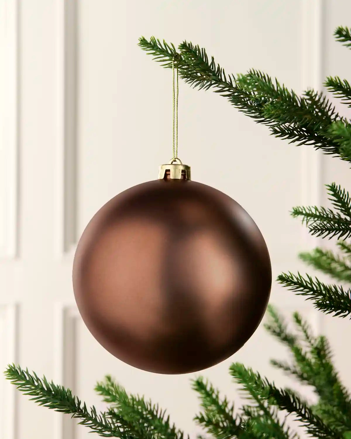 espresso oversized bauble hanging with gold string on a Christmas tree against a cream background