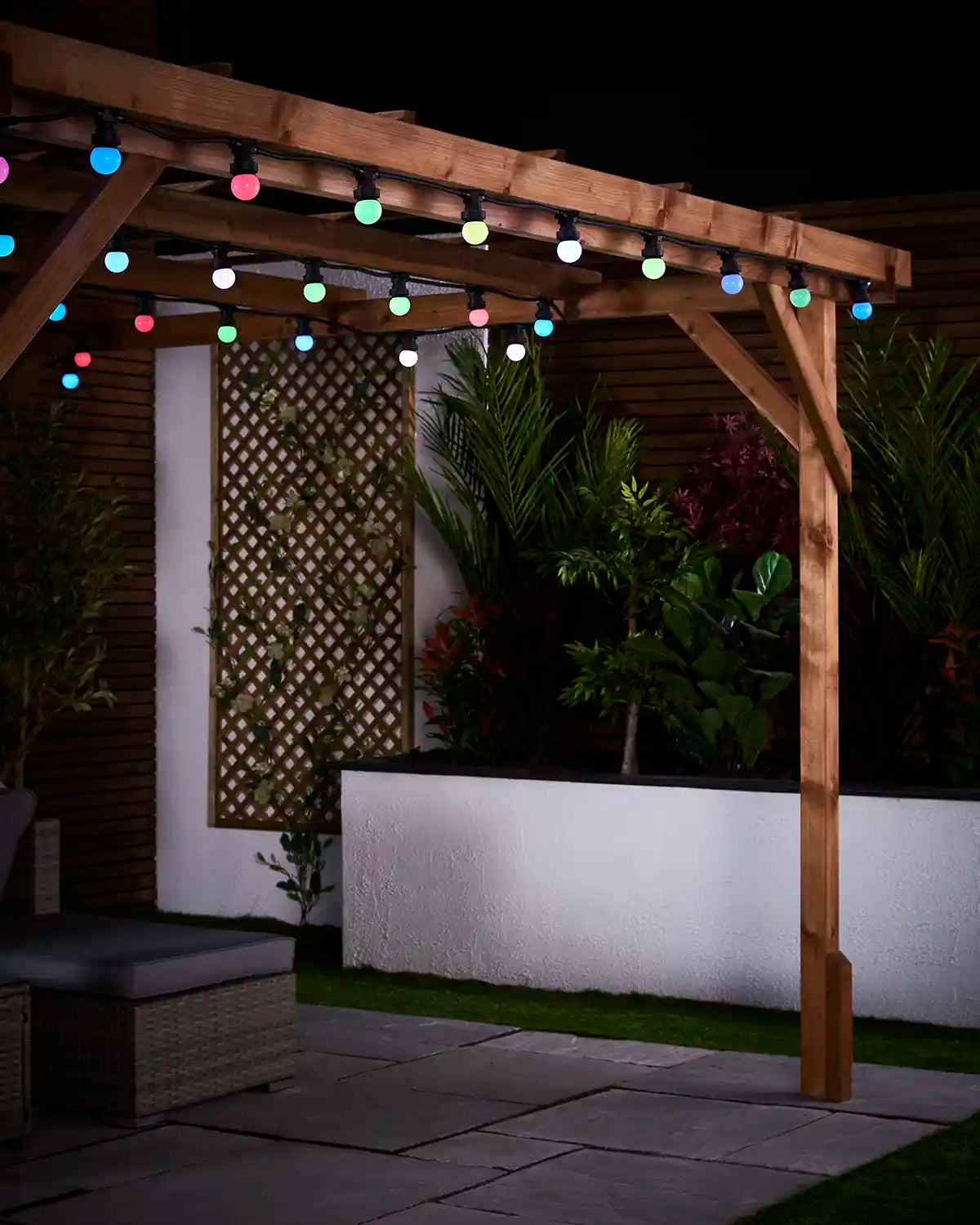 Multi-colour E27 festoon bulbs hanging from a wooden pergola in an outdoor garden setting.