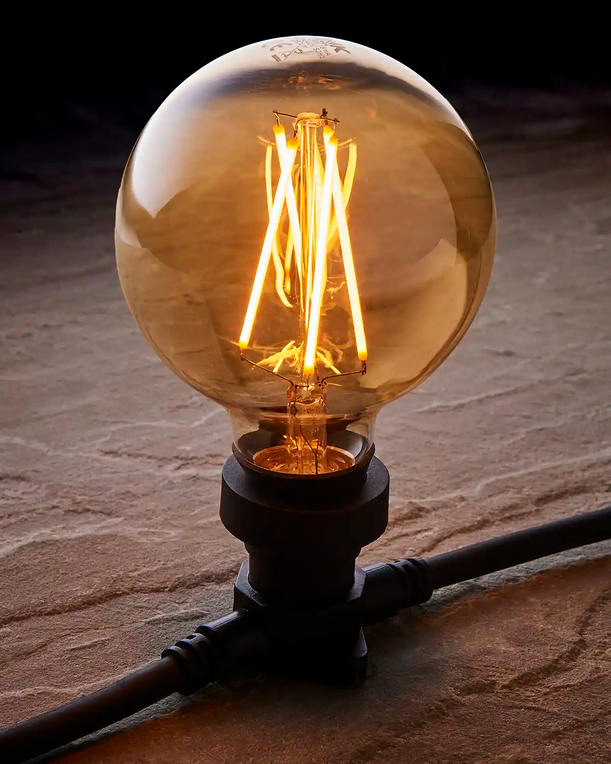 Close-up of a 4W E27 globe filament LED bulb with golden-tinted glass glowing warm white.