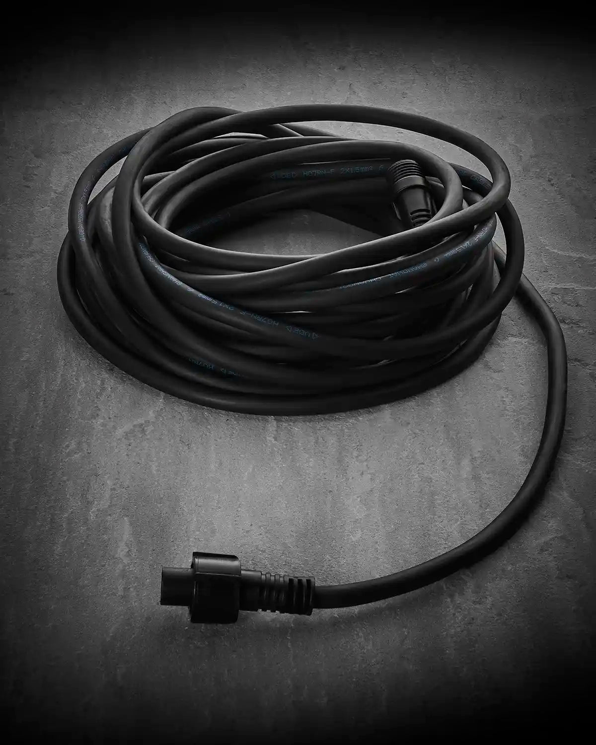 Coiled black Festoon Series connectable extension cable on a grey surface.