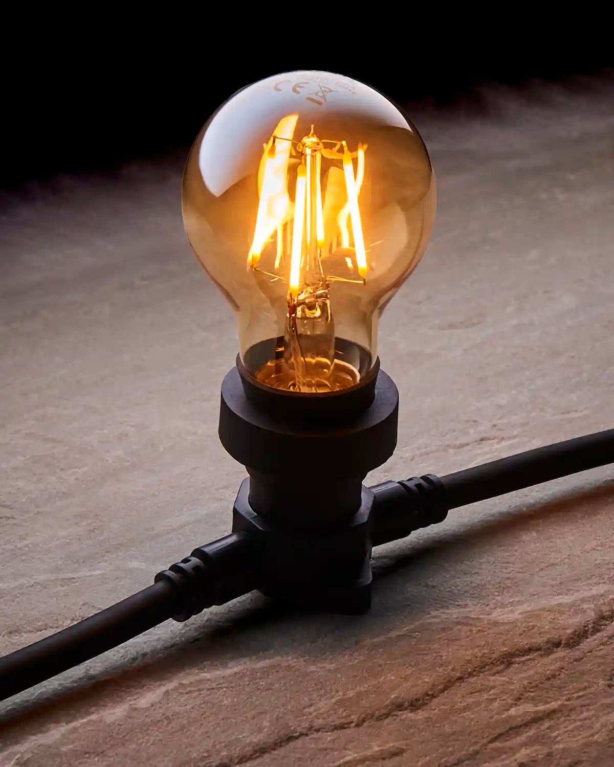 Close-up of a warm white E27 filament bulb with golden-tinted glass fitted into a black festoon belt.