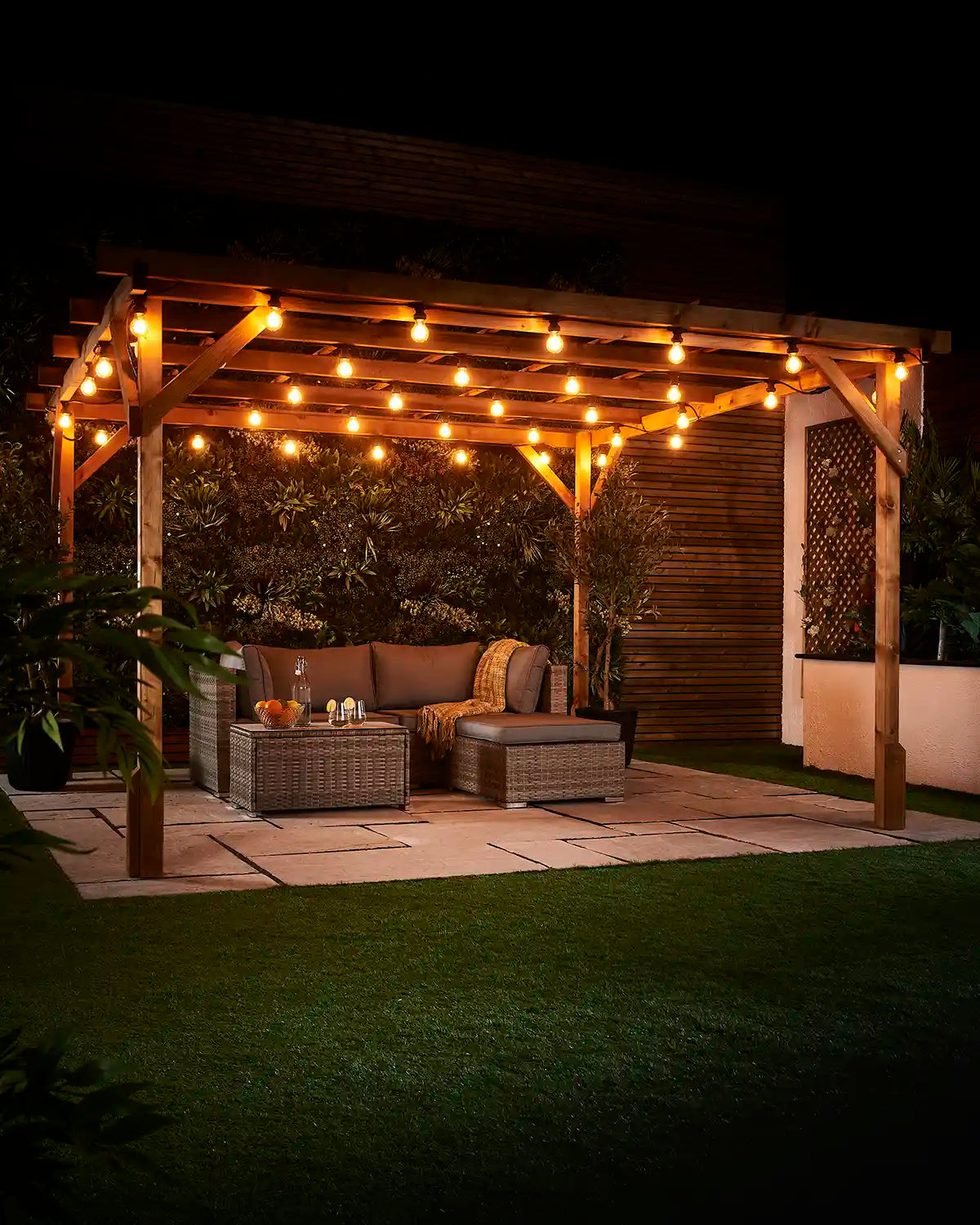 Warm white E27 filament bulbs hanging across a wooden pergola above an outdoor seating area at night.