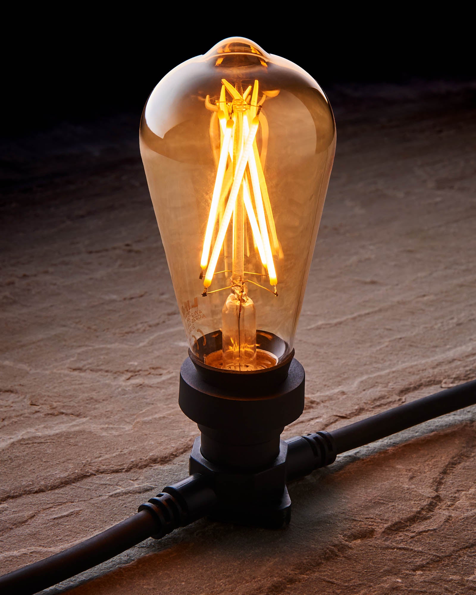 Close-up of a warm white E27 teardrop filament bulb with golden-tinted glass fitted into a black festoon belt.