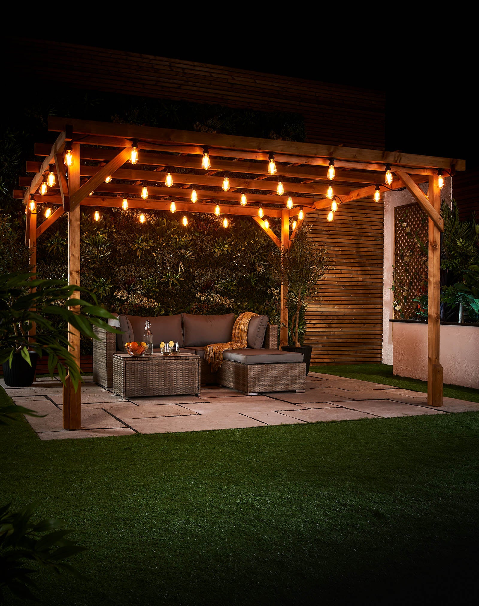 Warm white teardrop filament bulbs hanging across a wooden pergola above an outdoor seating area at night.