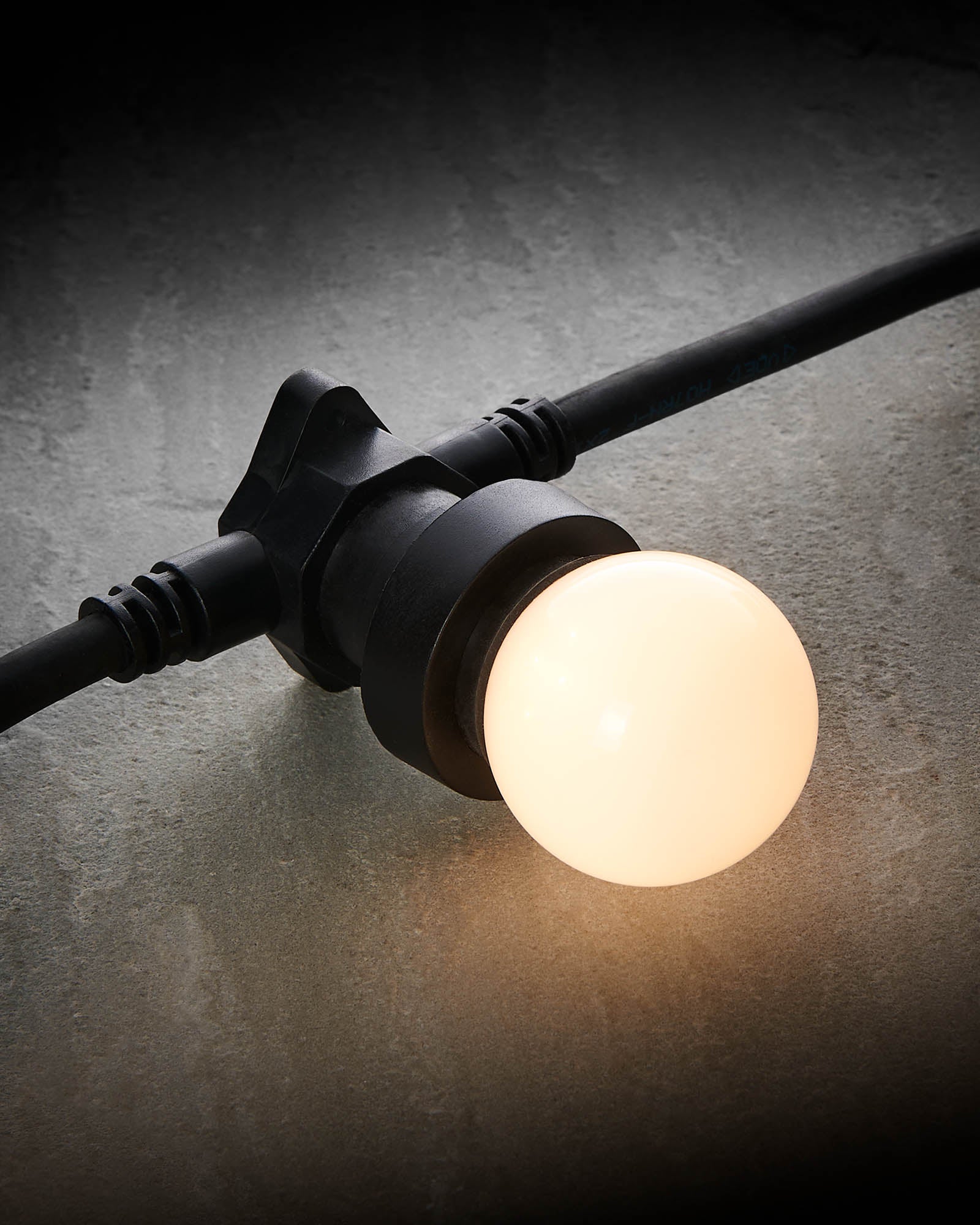 Warm white E27 LED festoon bulb glowing in a black festoon socket on a grey stone surface.