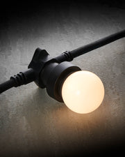 Warm white E27 LED festoon bulb glowing in a black festoon socket on a grey stone surface.