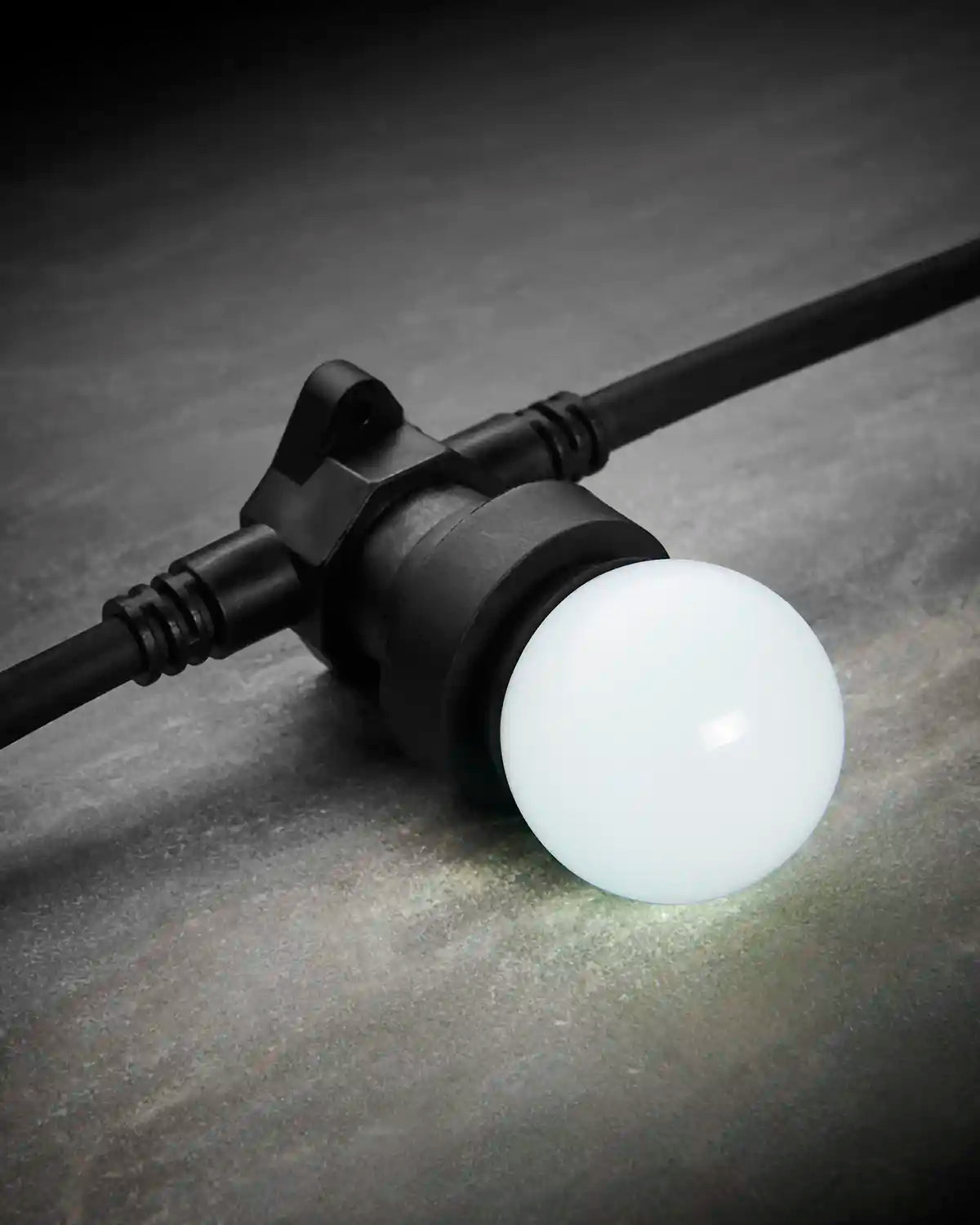 White E27 LED festoon bulb shown glowing in a black festoon socket on a dark stone surface.