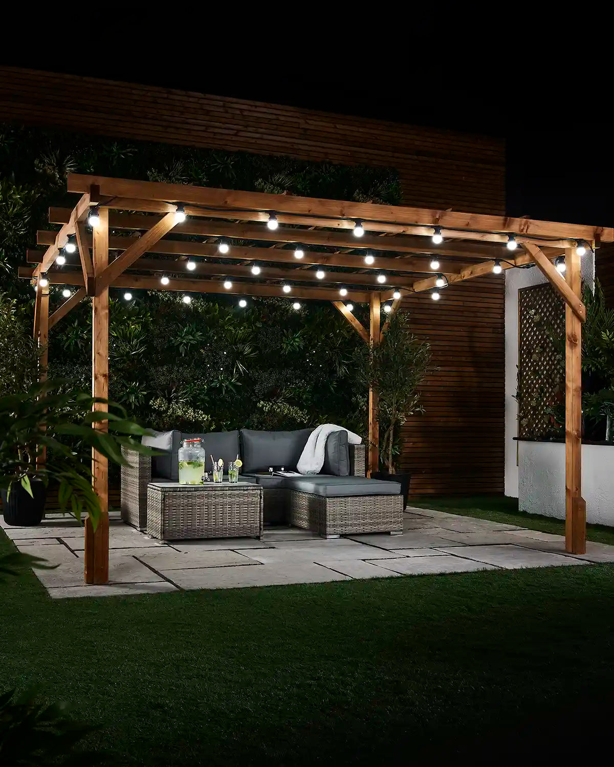White E27 festoon bulbs hanging from a wooden patio pergola above outdoor seating at night.