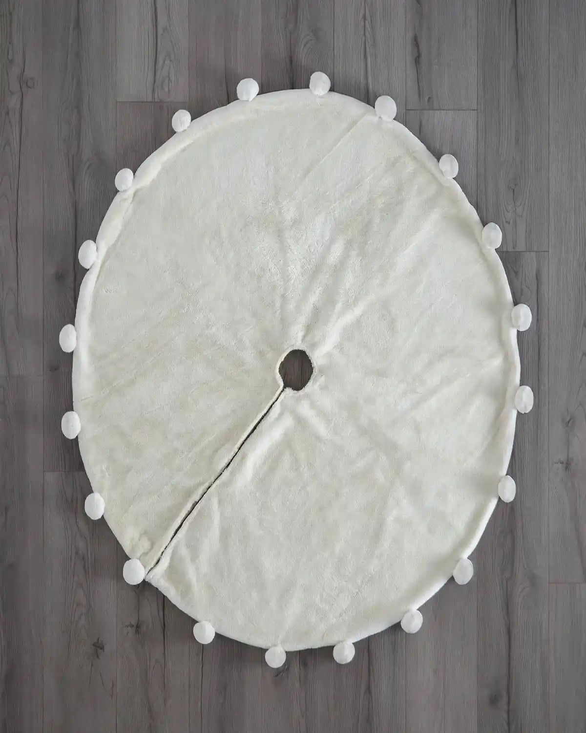 Top view of cream pom pom faux fur Christmas tree skirt on wooden floor