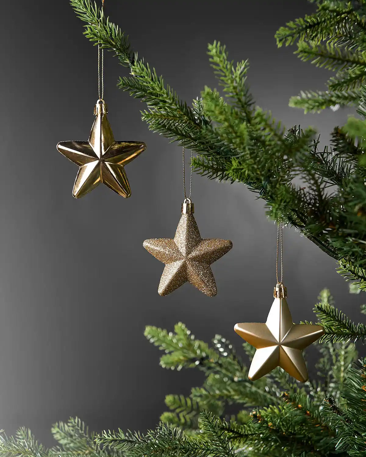 Gold 7cm hanging star decorations in shiny, glitter and matte finishes displayed on a Christmas tree.