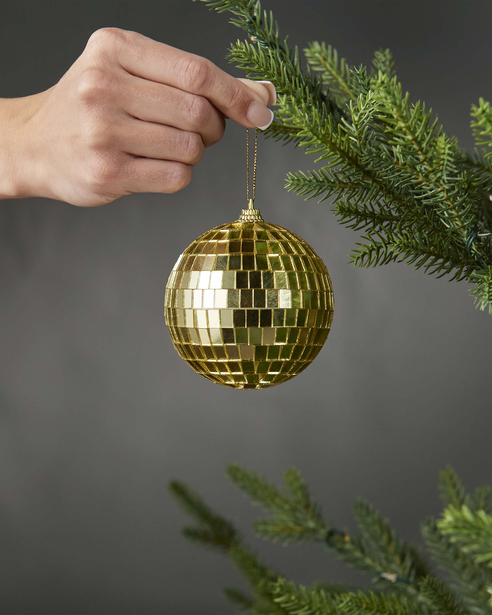 Hand holding a gold 8cm disco ball bauble beside a Christmas tree.