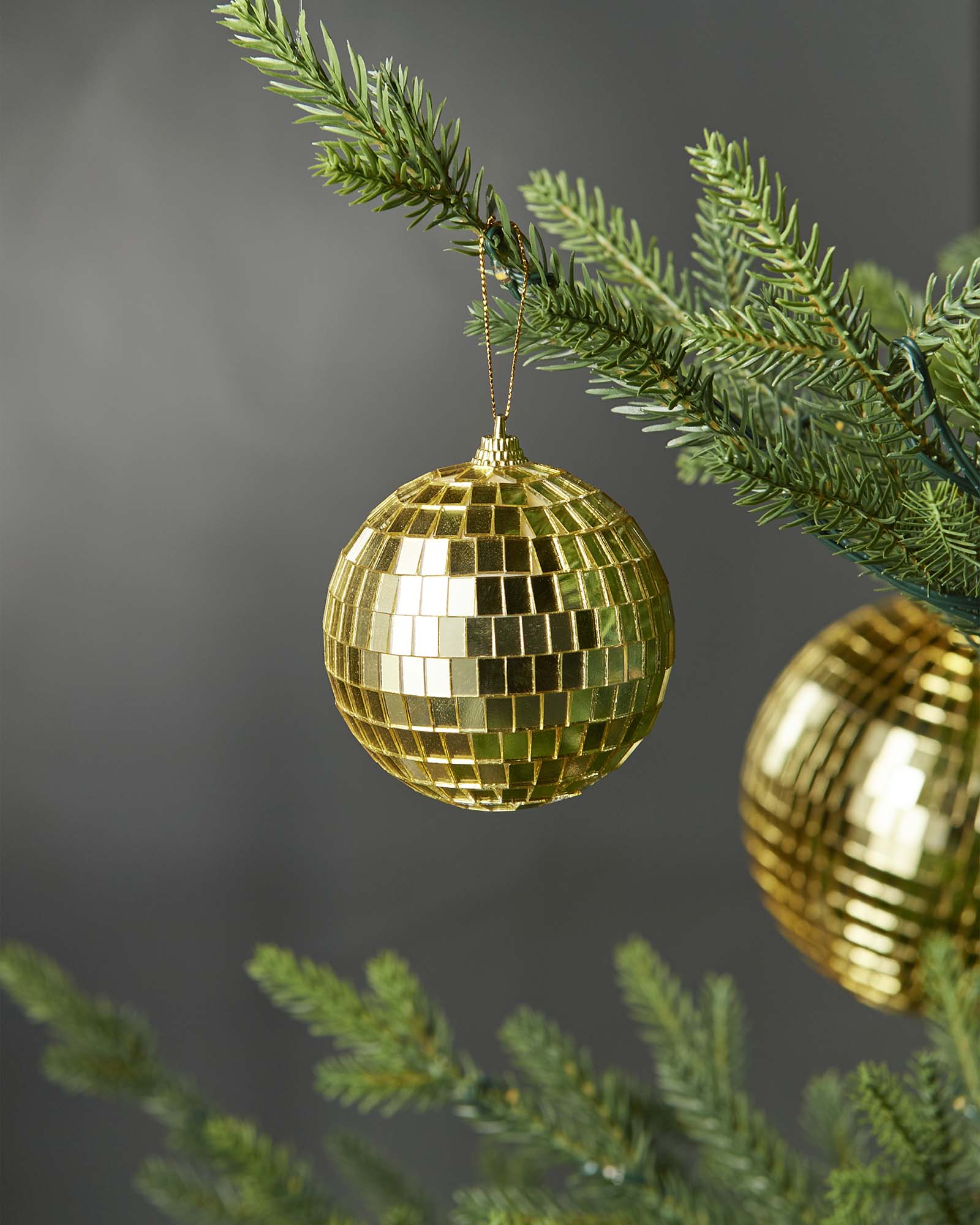 Gold 8cm disco ball bauble hanging on a Christmas tree branch.