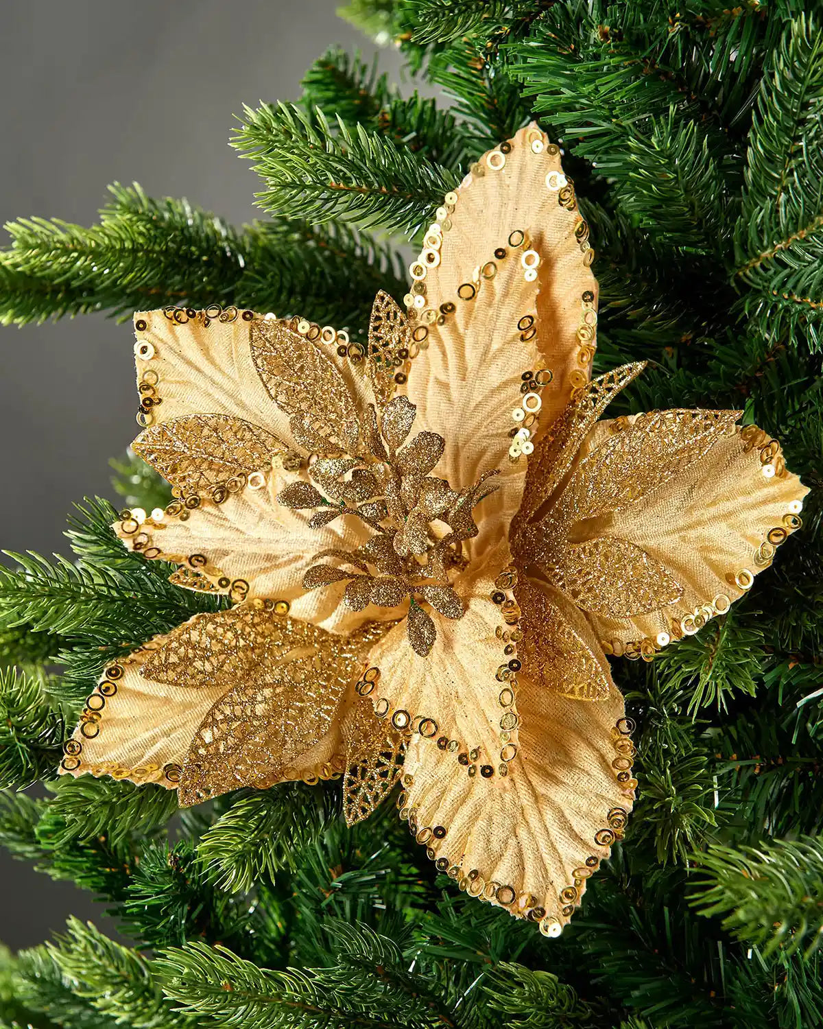 Gold artificial poinsettia flower with sequins, glittered lace petals and layered fabric petals displayed on a Christmas tree.