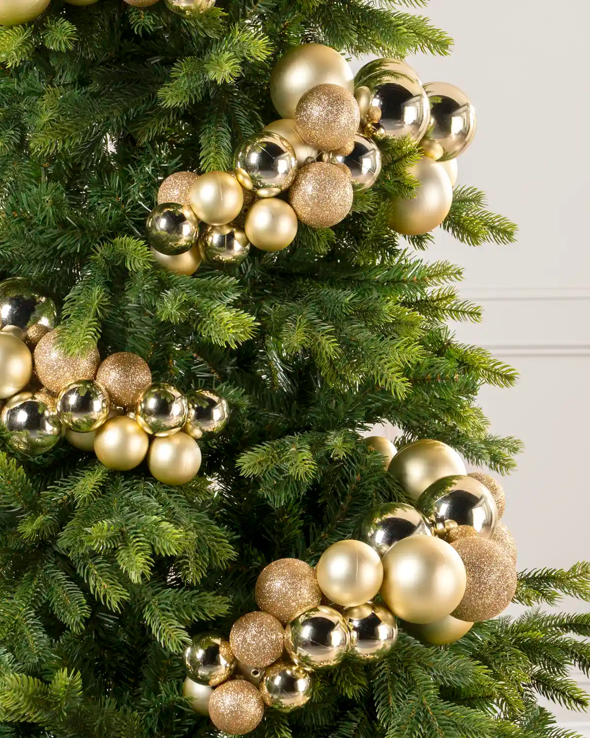 Close-up of gold bauble cluster arch on a Christmas tree showing mixed sizes and finishes.