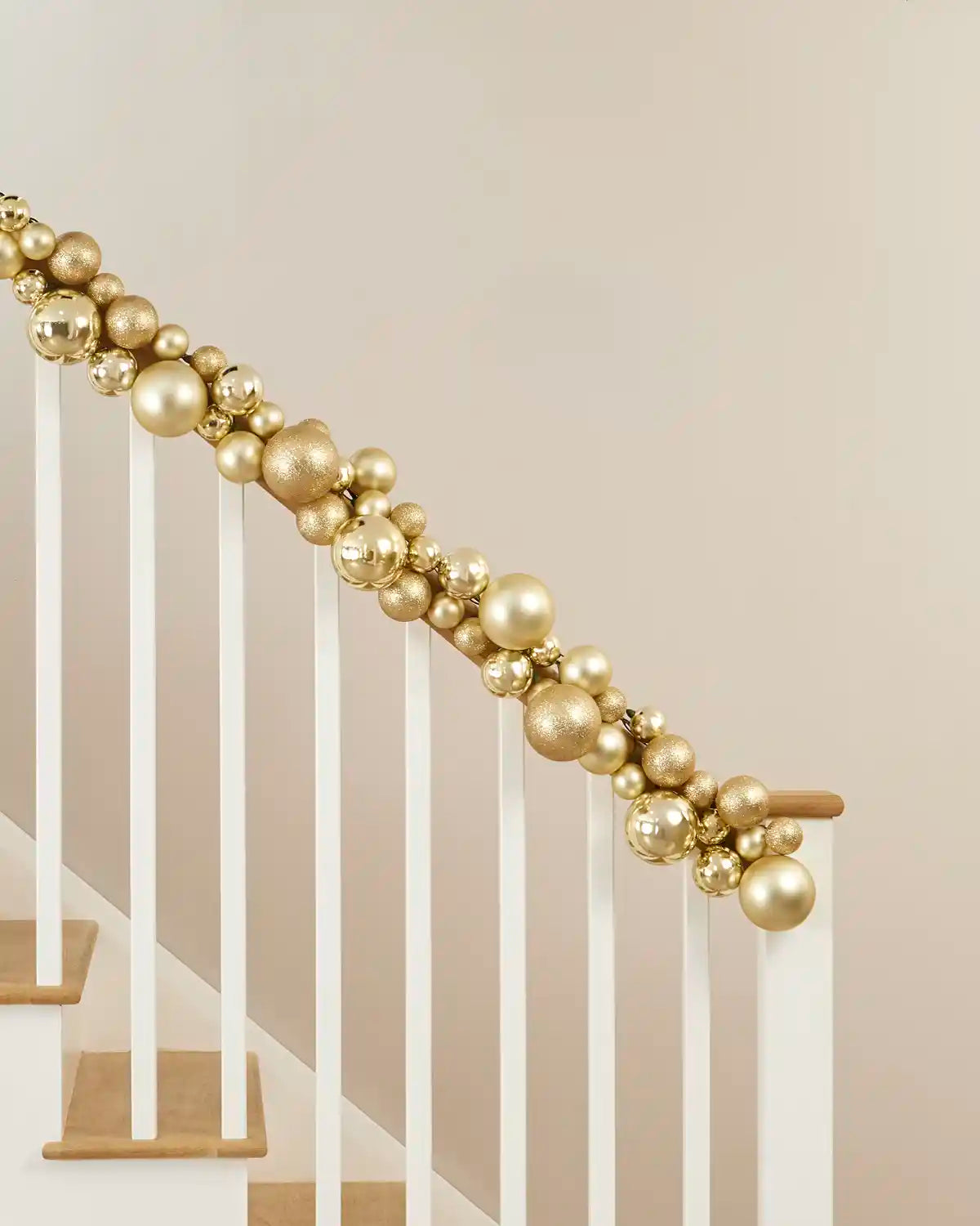 Gold bauble garland arranged along a staircase handrail with varied bauble sizes and finishes.
