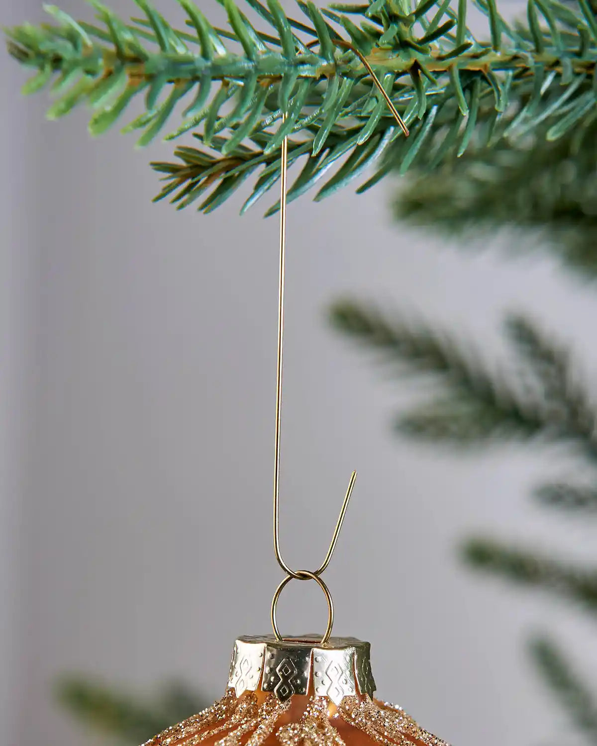 Gold bauble ornament hook attached to a Christmas tree branch