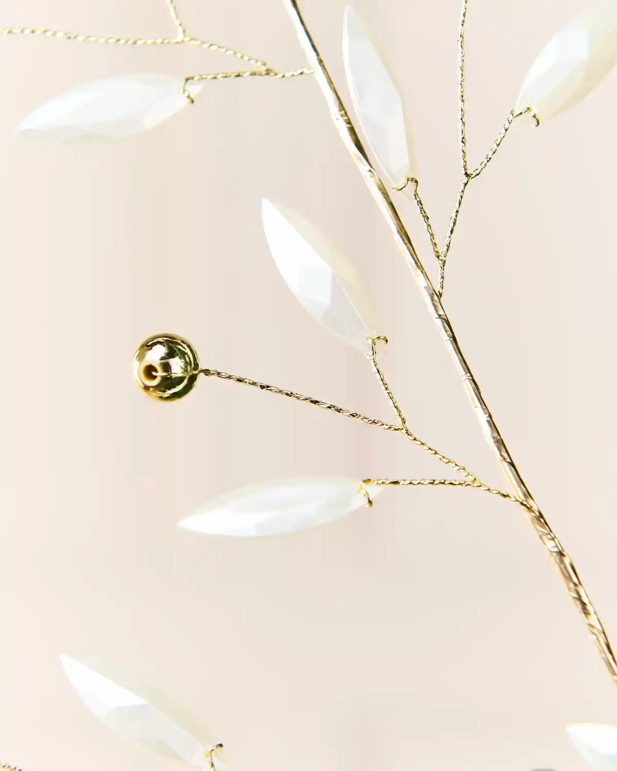 Detailed view of gold wire branches decorated with white pearl leaves and round gold beads.