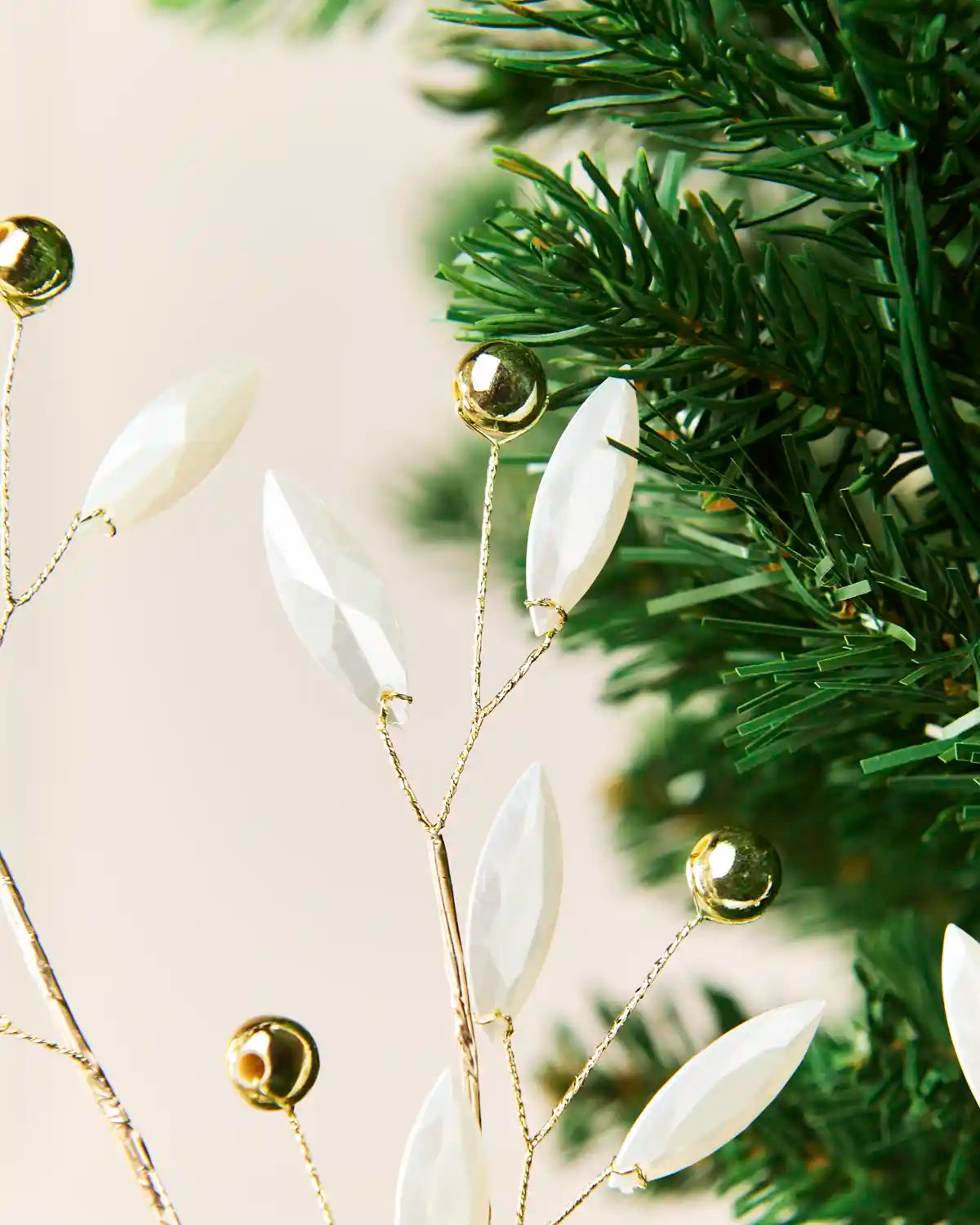 Close-up of white faceted pearl leaves and reflective gold beads on fine wire branches.