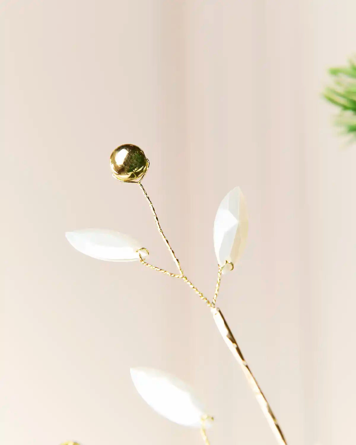 Close-up of a branch tip with two white pearl leaves and a reflective gold bead.