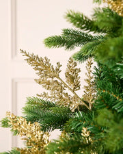 Gold glitter leaf pick arranged amongst green Christmas tree branches.