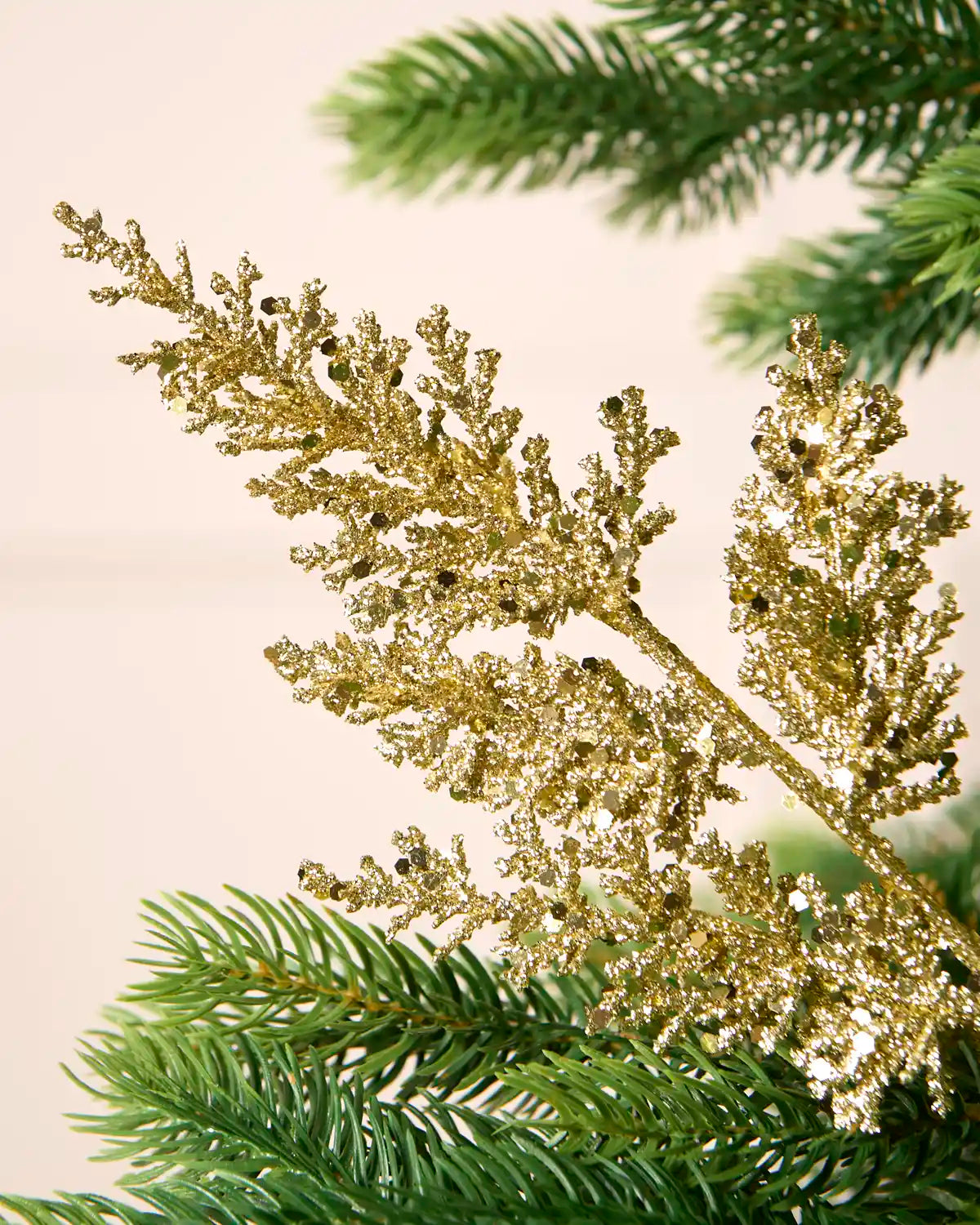 Close-up of a gold glitter leaf pick with reflective sequin detail amongst Christmas tree foliage.