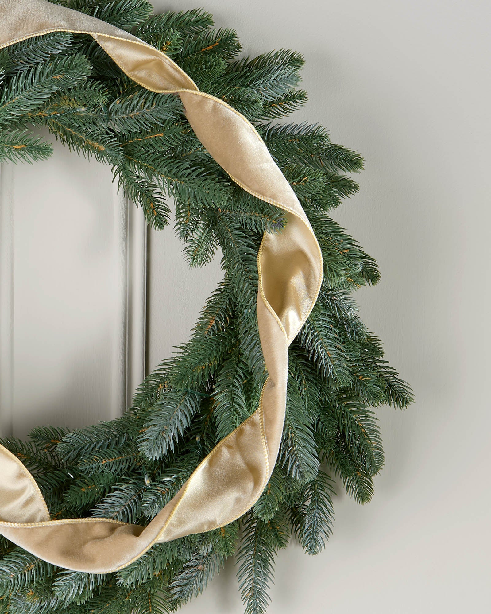 Gold velvet ribbon styled in a loose spiral on a green Christmas wreath.